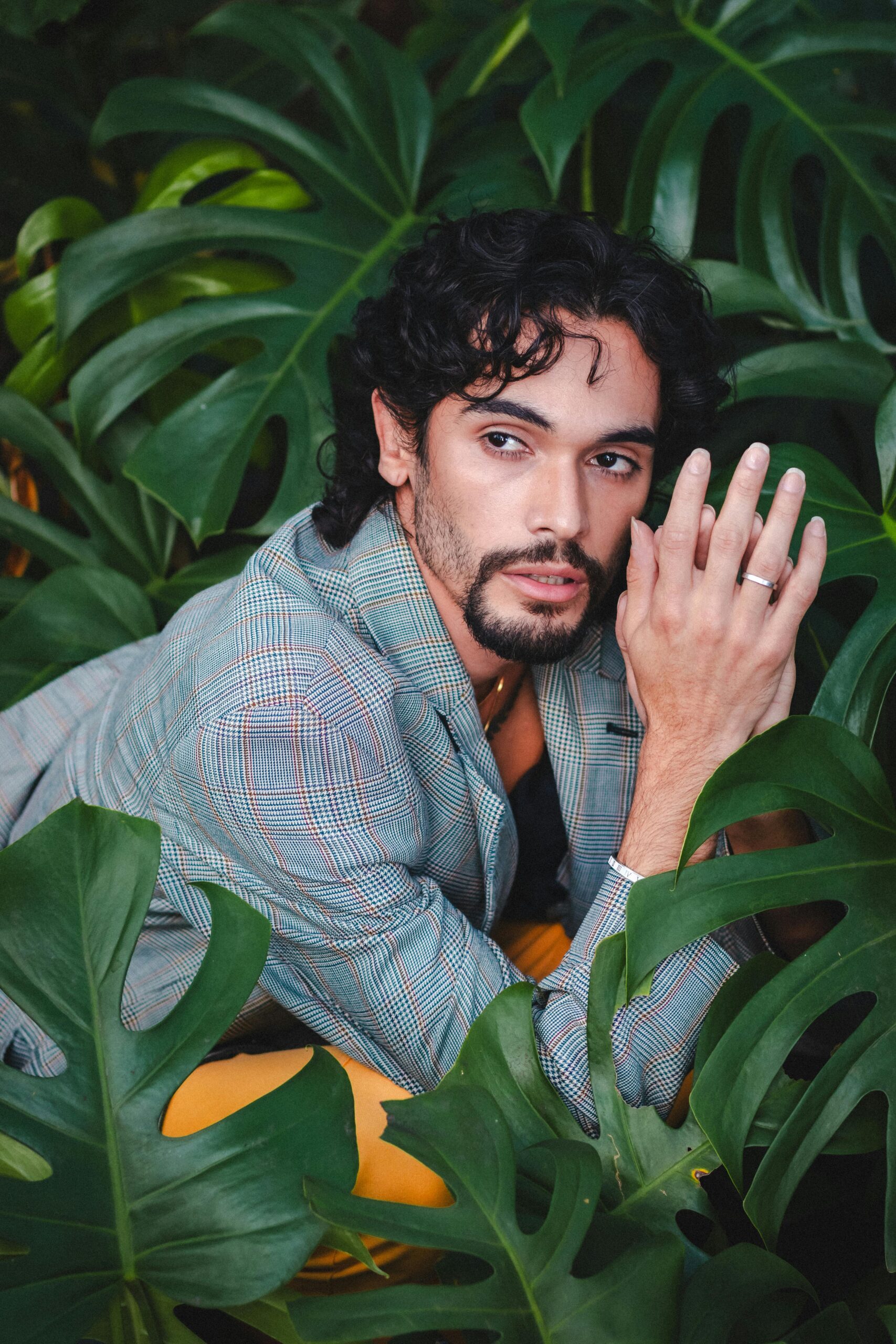 Man in a blazer poses surrounded by lush Monstera leaves, São Paulo inspired fashion shoot.